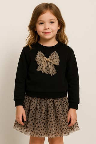 Young girl wearing a black sweater with a bow and a leopard print skirt on a plain background