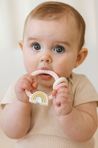Baby holding a rainbow teether against a plain background