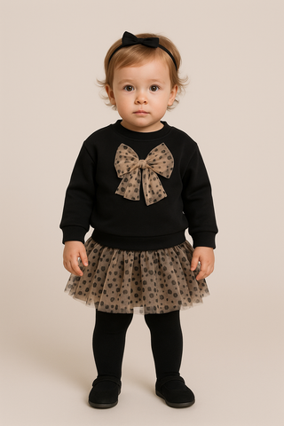 Child wearing a black sweater with a bow and a matching tutu skirt on a beige background